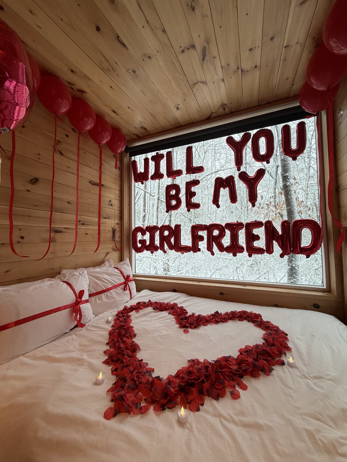 Romantic proposal setup with red rose petals forming a heart and a custom sign