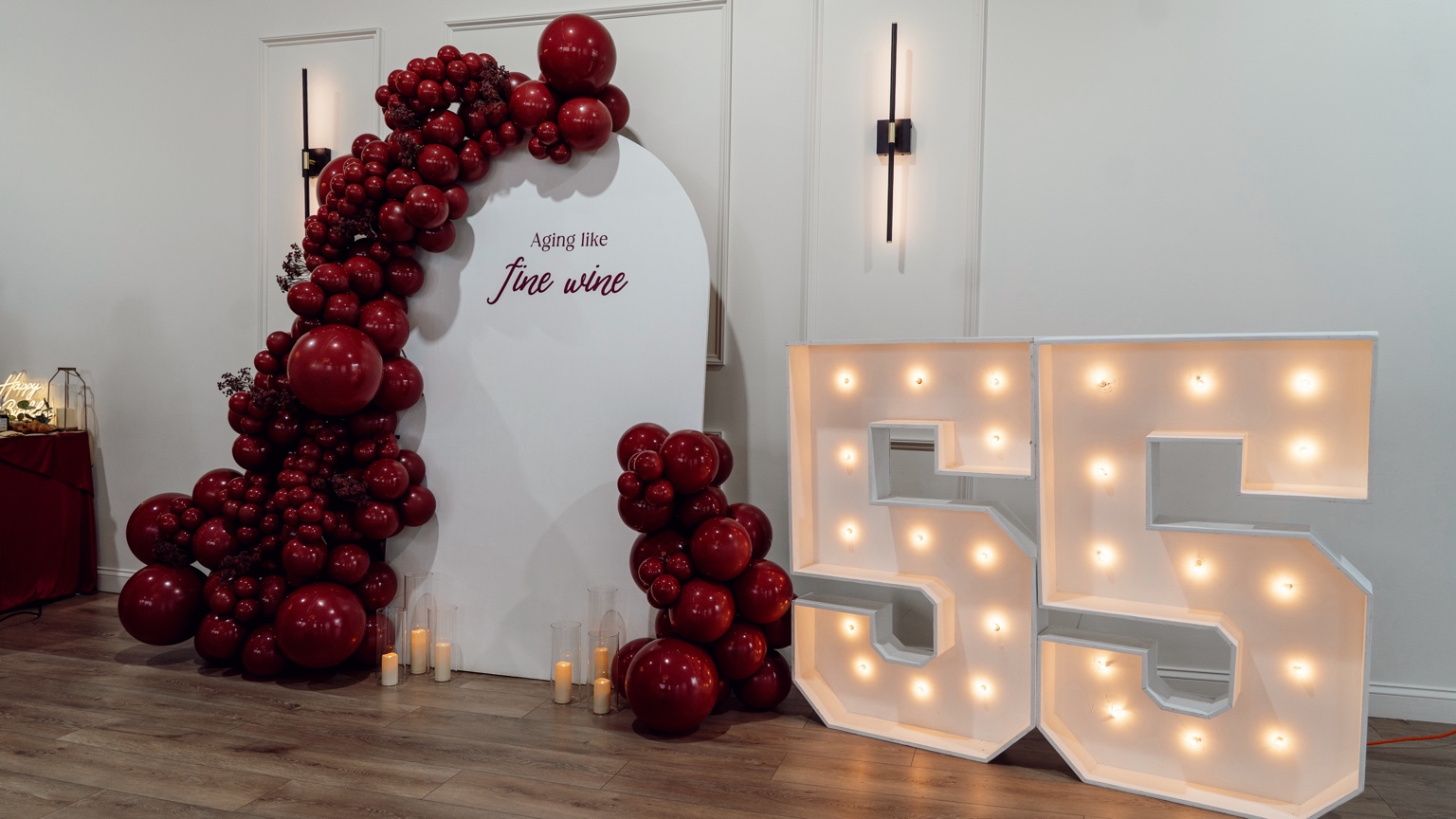 Burgundy balloon installation framing a milestone birthday backdrop and illuminated 55 numbers